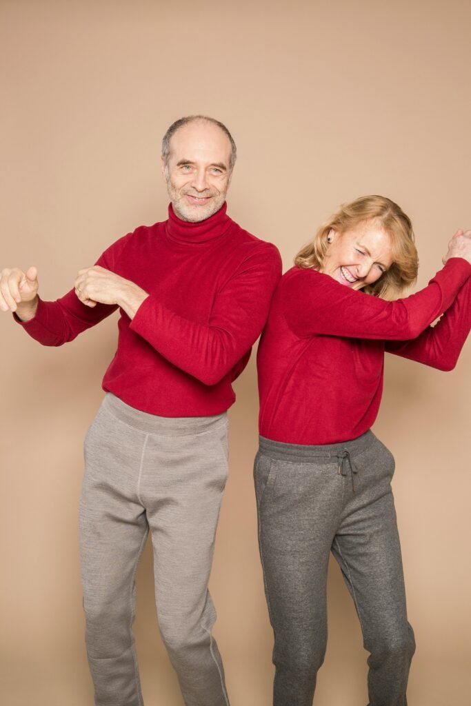 Energetic senior couple in matching red sweaters dancing happily indoors.